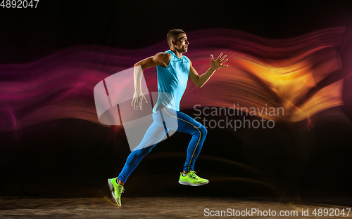 Image of Professional male runner training isolated on black studio background in mixed light