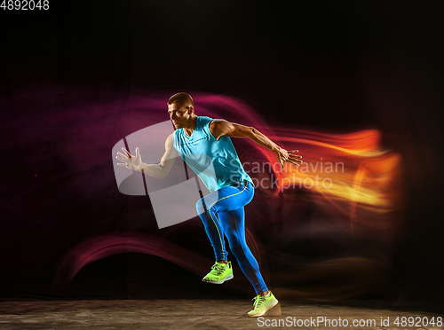 Image of Professional male runner training isolated on black studio background in mixed light