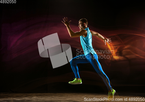 Image of Professional male runner training isolated on black studio background in mixed light