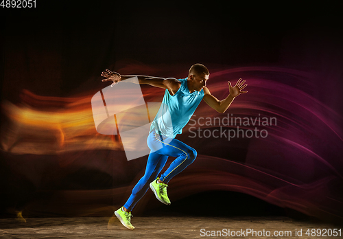Image of Professional male runner training isolated on black studio background in mixed light
