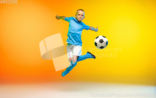 Image of Young boy as a soccer or football player in sportwear practicing on gradient yellow studio background in neon light