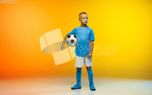 Image of Young boy as a soccer or football player in sportwear practicing on gradient yellow studio background in neon light