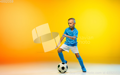 Image of Young boy as a soccer or football player in sportwear practicing on gradient yellow studio background in neon light