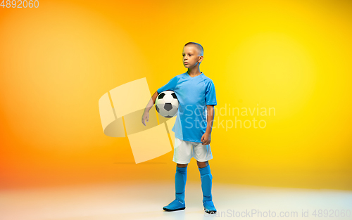 Image of Young boy as a soccer or football player in sportwear practicing on gradient yellow studio background in neon light