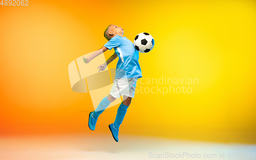 Image of Young boy as a soccer or football player in sportwear practicing on gradient yellow studio background in neon light