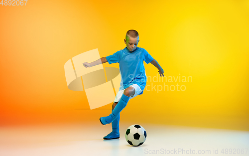 Image of Young boy as a soccer or football player in sportwear practicing on gradient yellow studio background in neon light