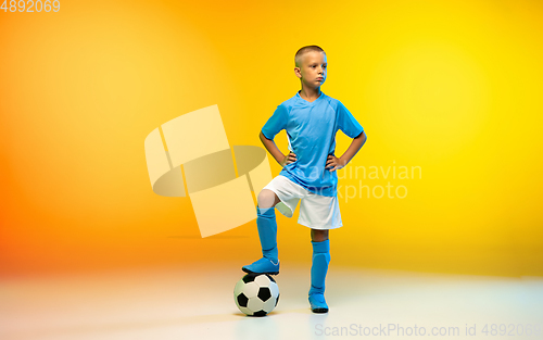 Image of Young boy as a soccer or football player in sportwear practicing on gradient yellow studio background in neon light