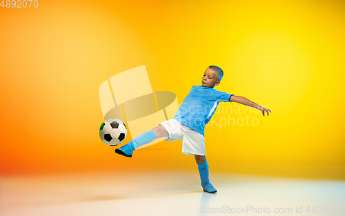 Image of Young boy as a soccer or football player in sportwear practicing on gradient yellow studio background in neon light