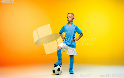 Image of Young boy as a soccer or football player in sportwear practicing on gradient yellow studio background in neon light