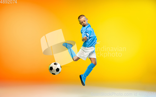 Image of Young boy as a soccer or football player in sportwear practicing on gradient yellow studio background in neon light