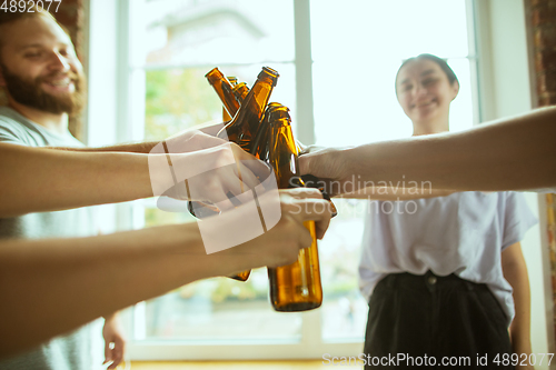 Image of Young group of friends drinking beer, having fun, laughting and celebrating together. Close up clinking beer bottles