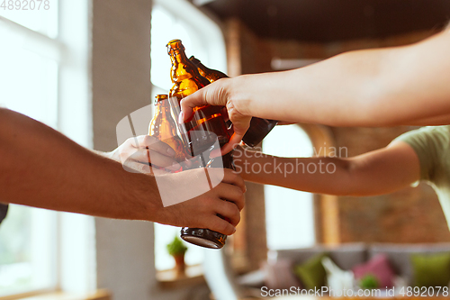 Image of Young group of friends drinking beer, having fun, laughting and celebrating together. Close up clinking beer bottles