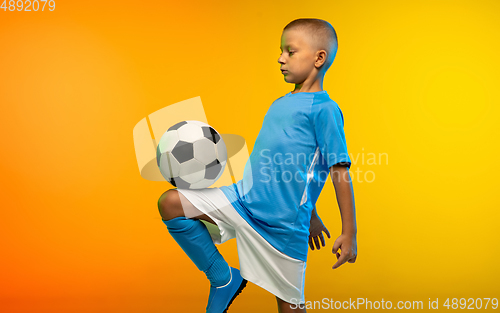 Image of Young boy as a soccer or football player in sportwear practicing on gradient yellow studio background in neon light