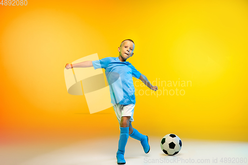 Image of Young boy as a soccer or football player in sportwear practicing on gradient yellow studio background in neon light
