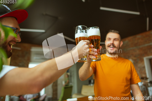 Image of Young group of friends drinking beer, having fun, laughting and celebrating together. Close up clinking beer bottles