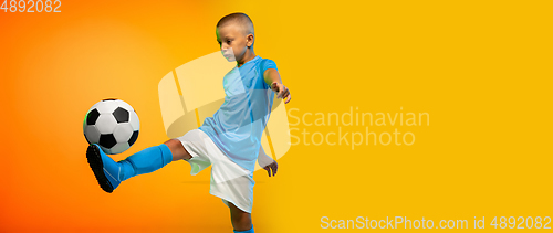 Image of Young boy as a soccer or football player in sportwear practicing on gradient yellow studio background in neon light