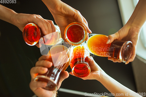 Image of Young group of friends drinking beer, having fun, laughting and celebrating together. Close up clinking beer glasses