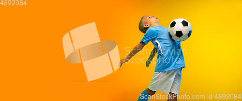 Image of Young boy as a soccer or football player in sportwear practicing on gradient yellow studio background in neon light