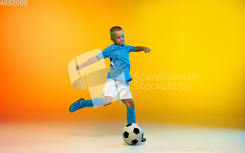 Image of Young boy as a soccer or football player in sportwear practicing on gradient yellow studio background in neon light