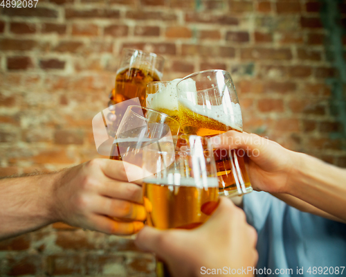 Image of Young group of friends drinking beer, having fun, laughting and celebrating together. Close up clinking beer glasses