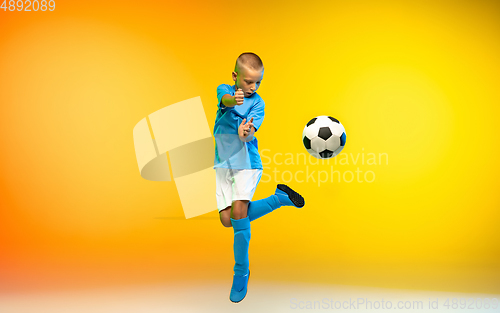 Image of Young boy as a soccer or football player in sportwear practicing on gradient yellow studio background in neon light