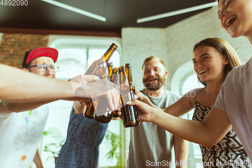 Image of Young group of friends drinking beer, having fun, laughting and celebrating together. Close up clinking beer bottles