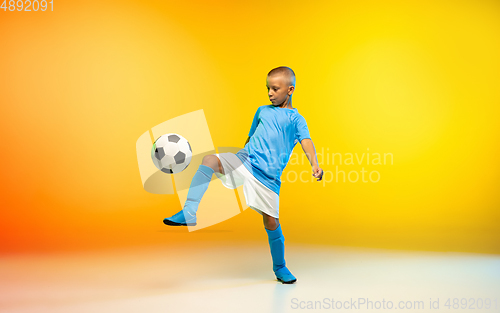 Image of Young boy as a soccer or football player in sportwear practicing on gradient yellow studio background in neon light