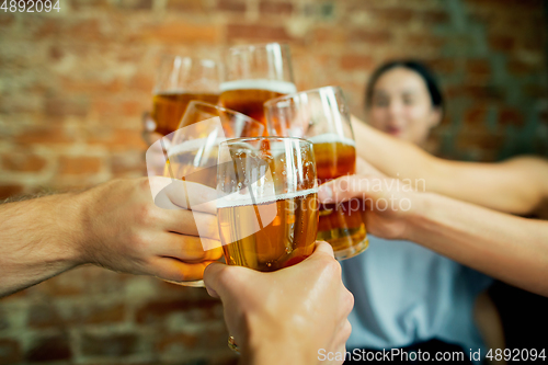 Image of Young group of friends drinking beer, having fun, laughting and celebrating together. Close up clinking beer glasses