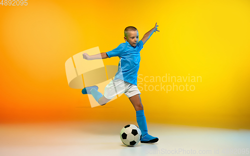 Image of Young boy as a soccer or football player in sportwear practicing on gradient yellow studio background in neon light