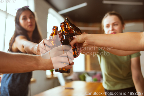 Image of Young group of friends drinking beer, having fun, laughting and celebrating together. Close up clinking beer bottles