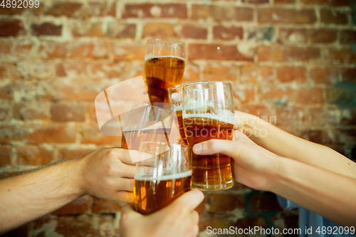 Image of Young group of friends drinking beer, having fun, laughting and celebrating together. Close up clinking beer glasses