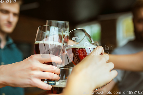 Image of Young group of friends drinking beer, having fun, laughting and celebrating together. Close up clinking beer glasses