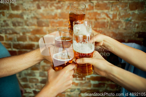 Image of Young group of friends drinking beer, having fun, laughting and celebrating together. Close up clinking beer glasses