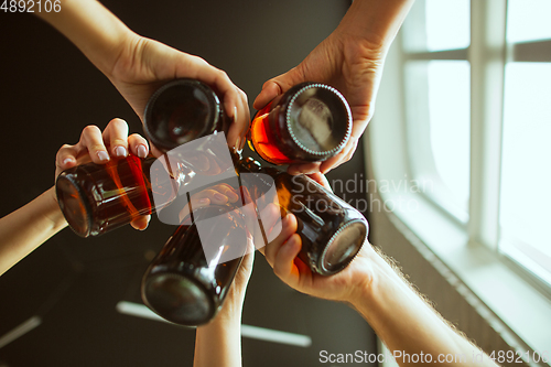 Image of Young group of friends drinking beer, having fun, laughting and celebrating together. Close up clinking beer bottles