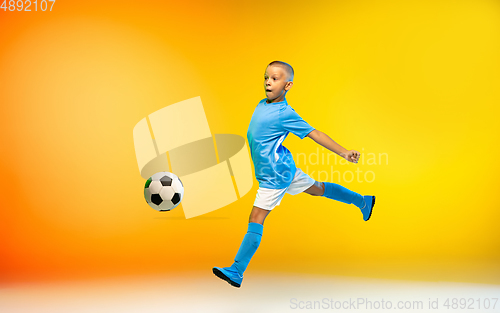 Image of Young boy as a soccer or football player in sportwear practicing on gradient yellow studio background in neon light