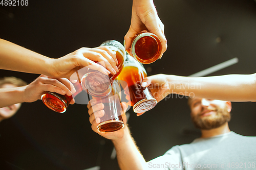 Image of Young group of friends drinking beer, having fun, laughting and celebrating together. Close up clinking beer glasses