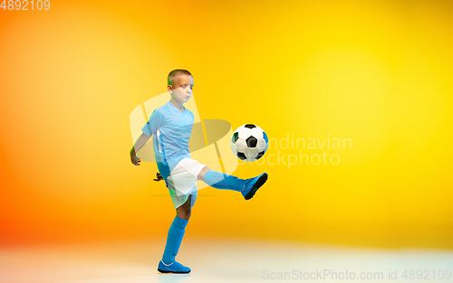 Image of Young boy as a soccer or football player in sportwear practicing on gradient yellow studio background in neon light