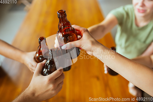 Image of Young group of friends drinking beer, having fun, laughting and celebrating together. Close up clinking beer bottles