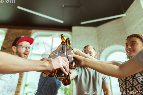 Image of Young group of friends drinking beer, having fun, laughting and celebrating together. Close up clinking beer bottles