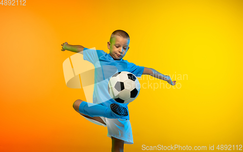 Image of Young boy as a soccer or football player in sportwear practicing on gradient yellow studio background in neon light
