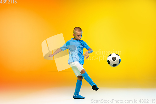 Image of Young boy as a soccer or football player in sportwear practicing on gradient yellow studio background in neon light