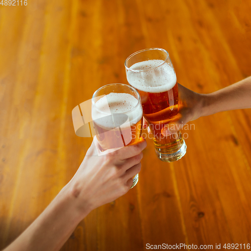 Image of Young group of friends drinking beer, having fun, laughting and celebrating together. Close up clinking beer glasses