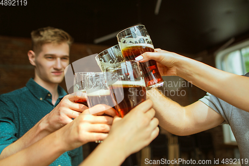 Image of Young group of friends drinking beer, having fun, laughting and celebrating together. Close up clinking beer glasses