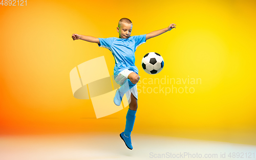 Image of Young boy as a soccer or football player in sportwear practicing on gradient yellow studio background in neon light