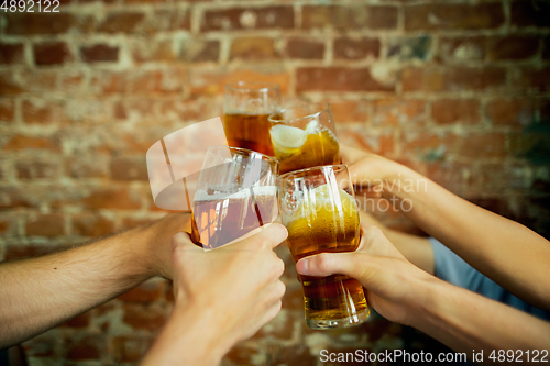 Image of Young group of friends drinking beer, having fun, laughting and celebrating together. Close up clinking beer glasses