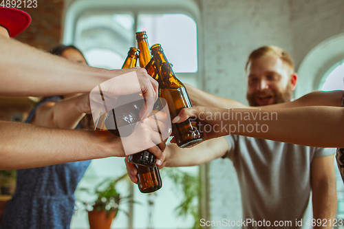 Image of Young group of friends drinking beer, having fun, laughting and celebrating together. Close up clinking beer bottles