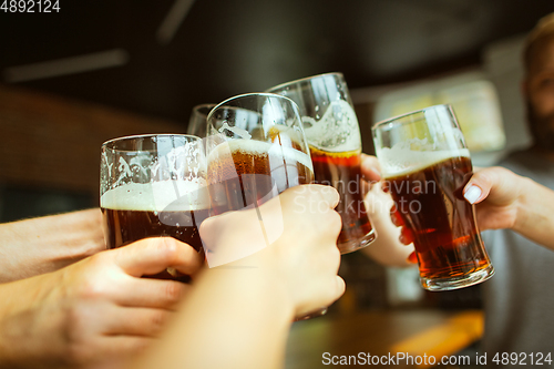 Image of Young group of friends drinking beer, having fun, laughting and celebrating together. Close up clinking beer glasses