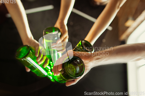 Image of Young group of friends drinking beer, having fun, laughting and celebrating together. Close up clinking beer bottles