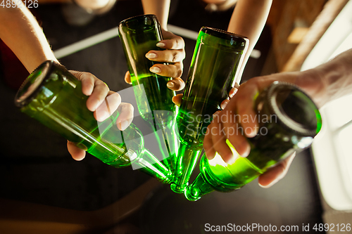 Image of Young group of friends drinking beer, having fun, laughting and celebrating together. Close up clinking beer bottles