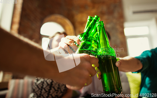 Image of Young group of friends drinking beer, having fun, laughting and celebrating together. Close up clinking beer bottles